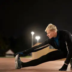 Mężczyzna rozciąga się na bieżni nocą. Dobre przygotowanie do biegania przed snem.
