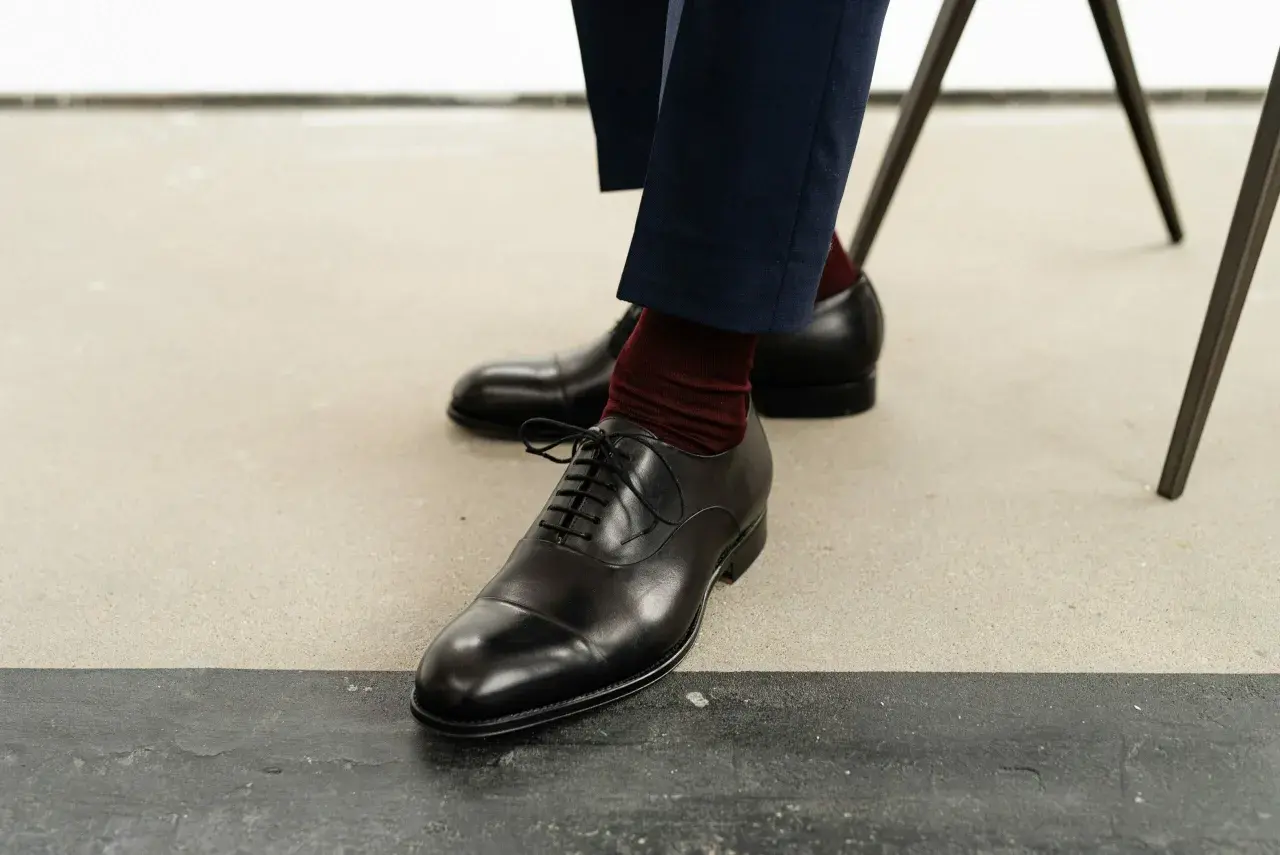 Eleganckie oksfordy, jedne z klasycznych rodzajów butów męskich, w połączeniu z bordowymi skarpetkami i granatowymi spodniami.